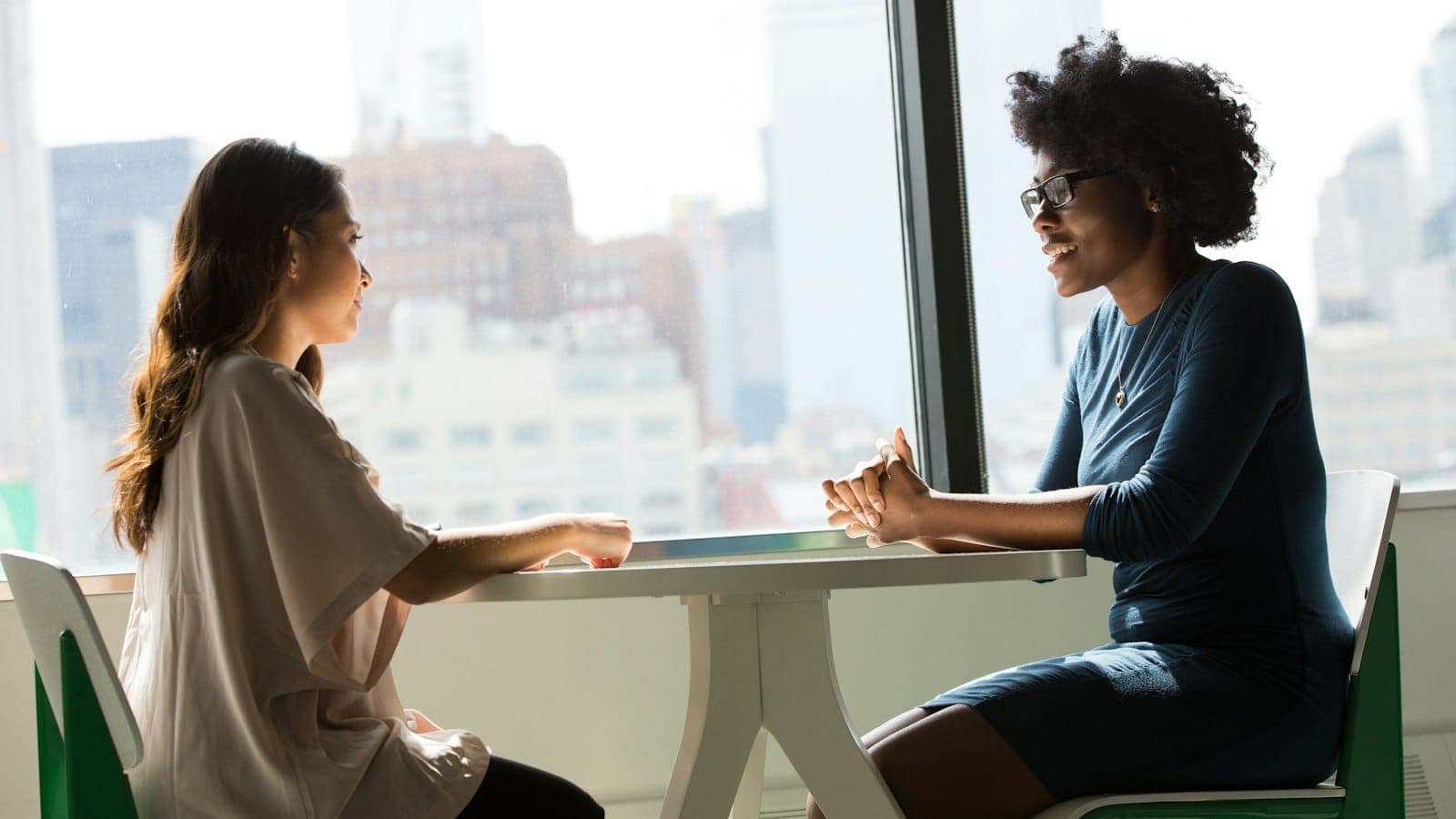 Two women sitting at a table in a friendly, supportive conversation in natural light