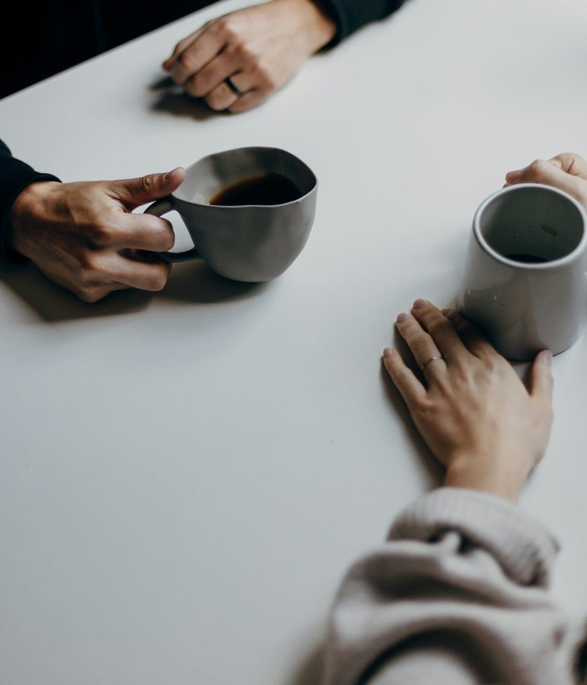 Two people leaning in over coffee cups at a table, mid-conversation in soft natural light
