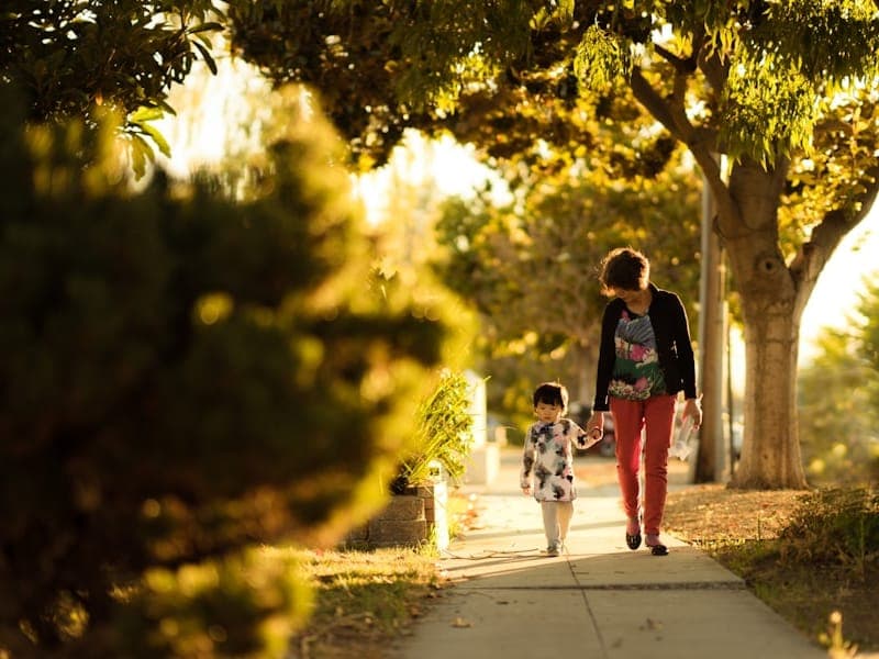 A woman and child seen from behind, walking hand in hand along a path at golden hour