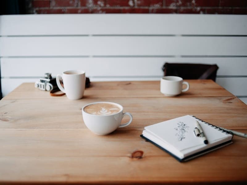 Two cups of coffee on a wooden table in soft window light, suggesting a gentle catch-up