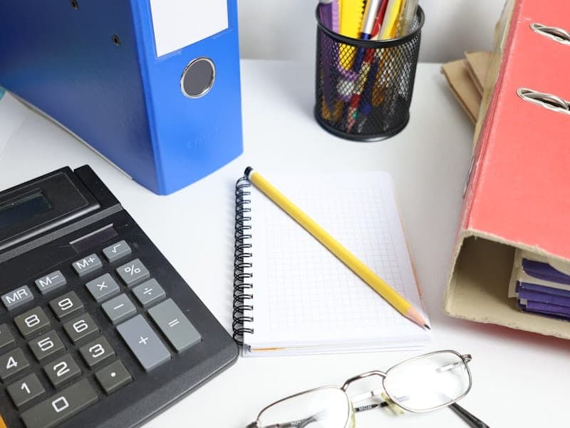 A tidy desk flat lay with binders, a notebook, calculator and glasses, neatly organised