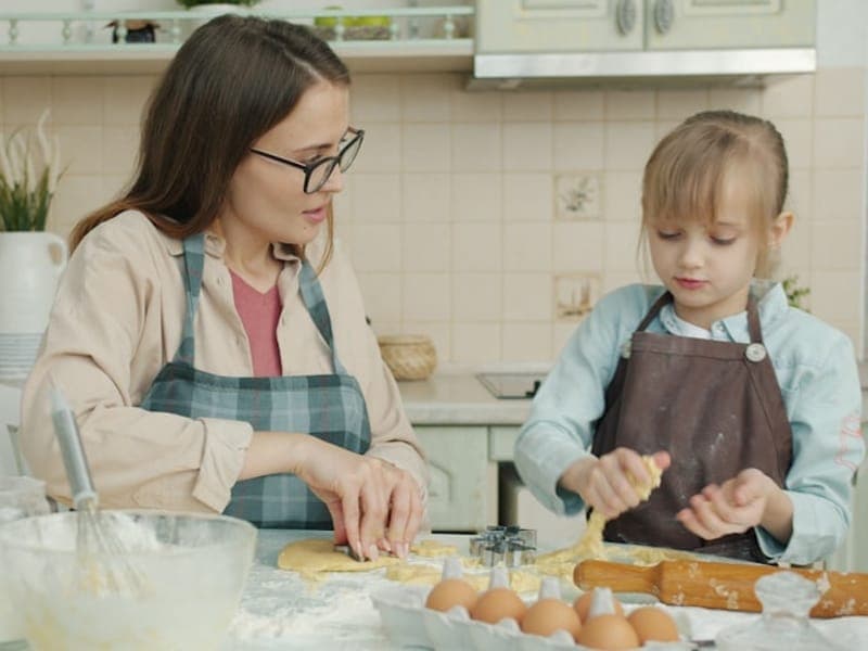 An adult and a child baking together in a warm home kitchen